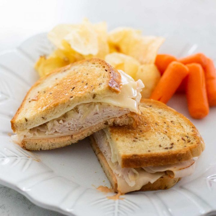 A grilled turkey reuben sandwich is on a plate with potato chips and baby carrots.