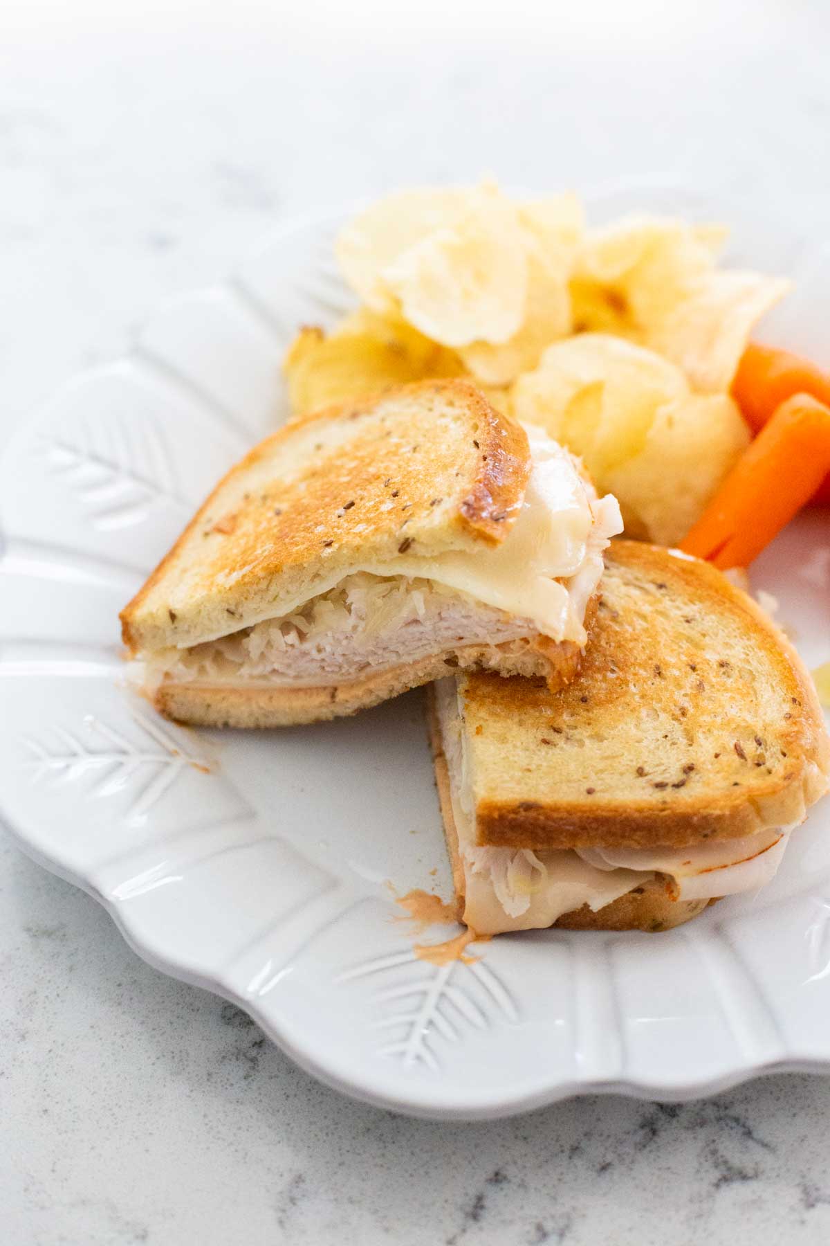 The finished turkey reuben is on a plate with potato chips and carrots.