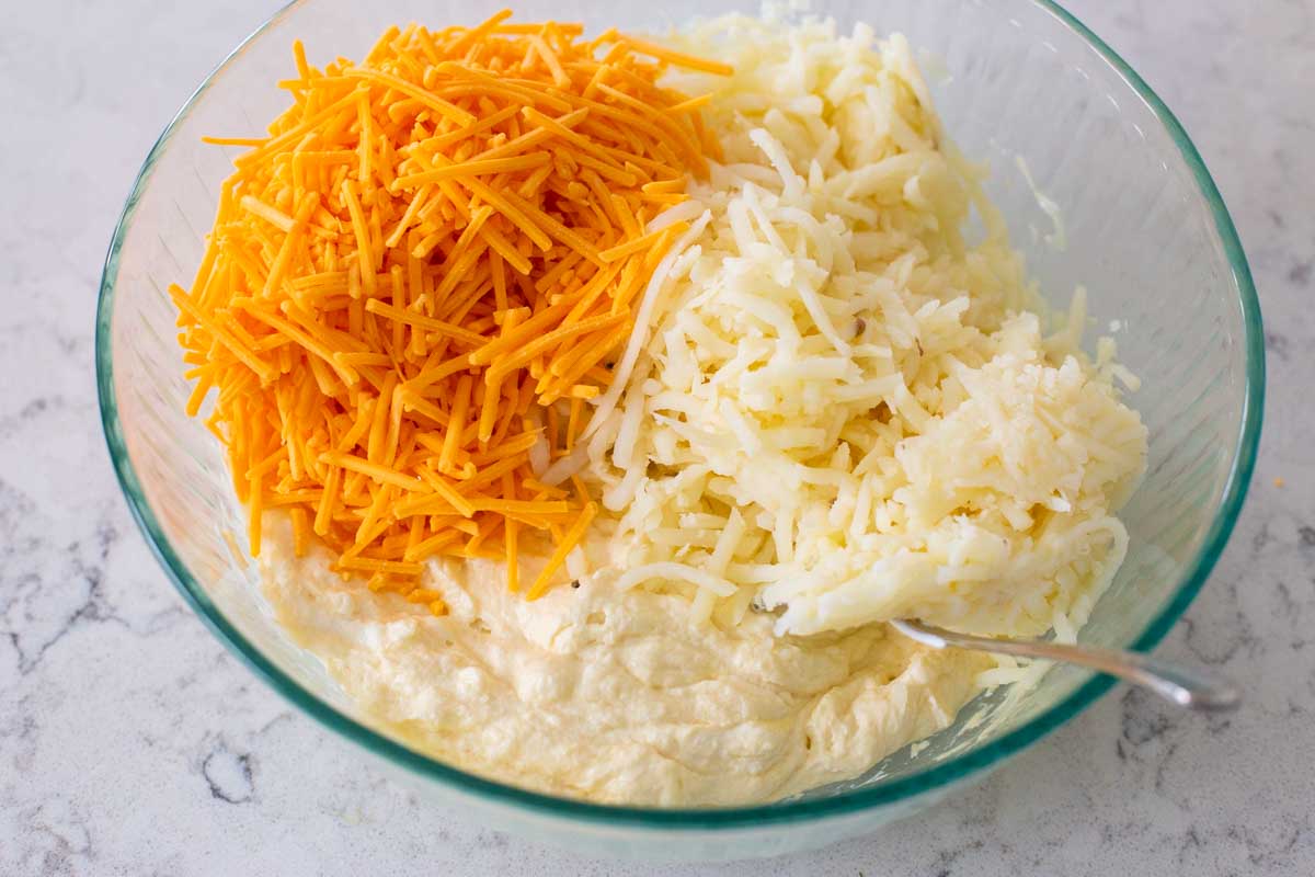The shredded cheese, cream of chicken soup, hashbrown potatoes, and other ingredients are in a mixing bowl.