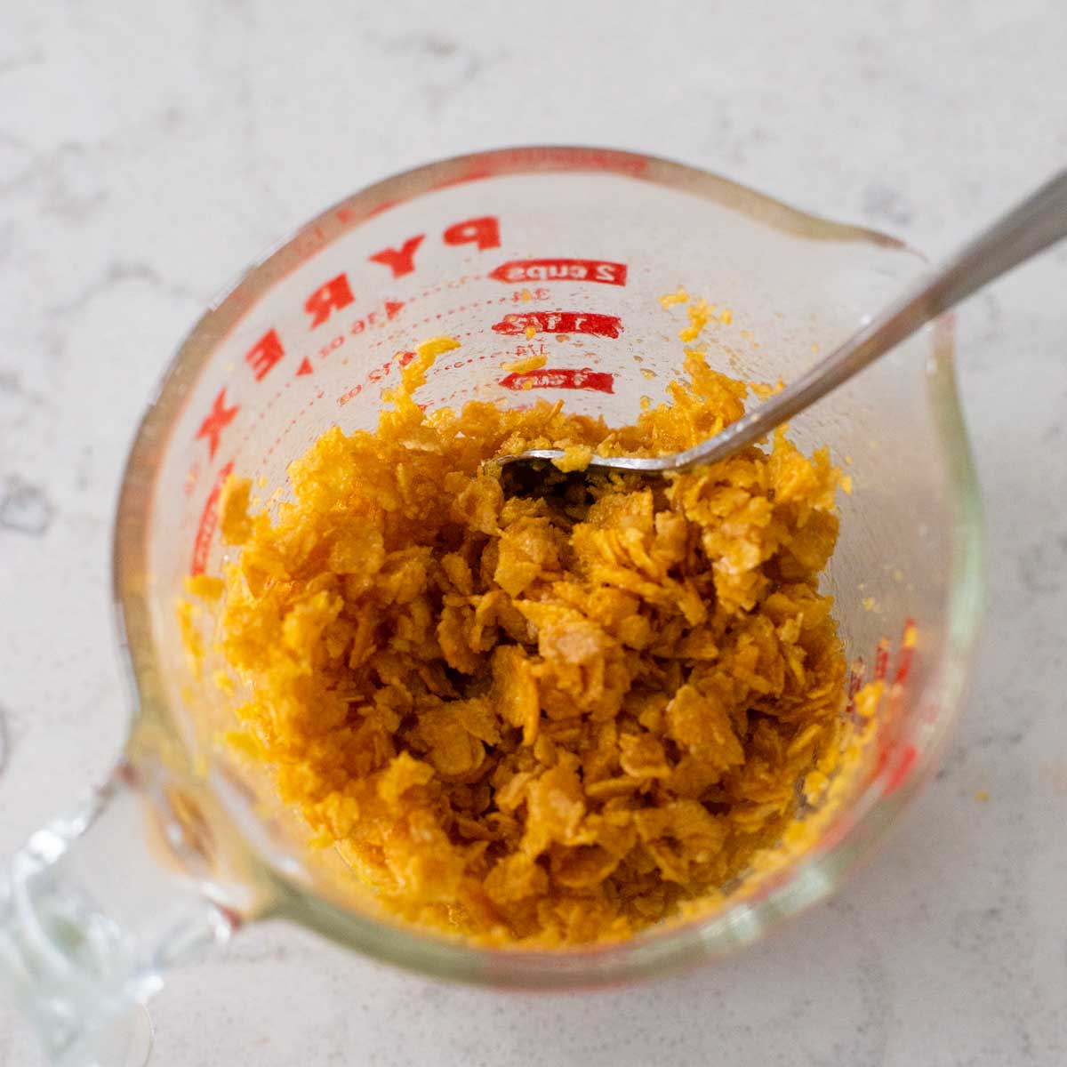 The crushed cornflakes have been mixed with melted butter in a measuring cup.
