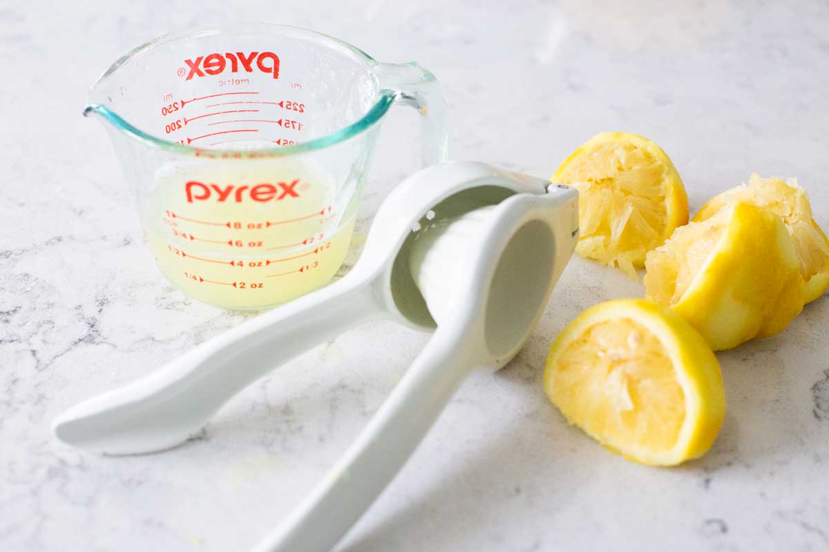 The citrus juicer has squeezed the lemon halves into a small liquid measuring cup.