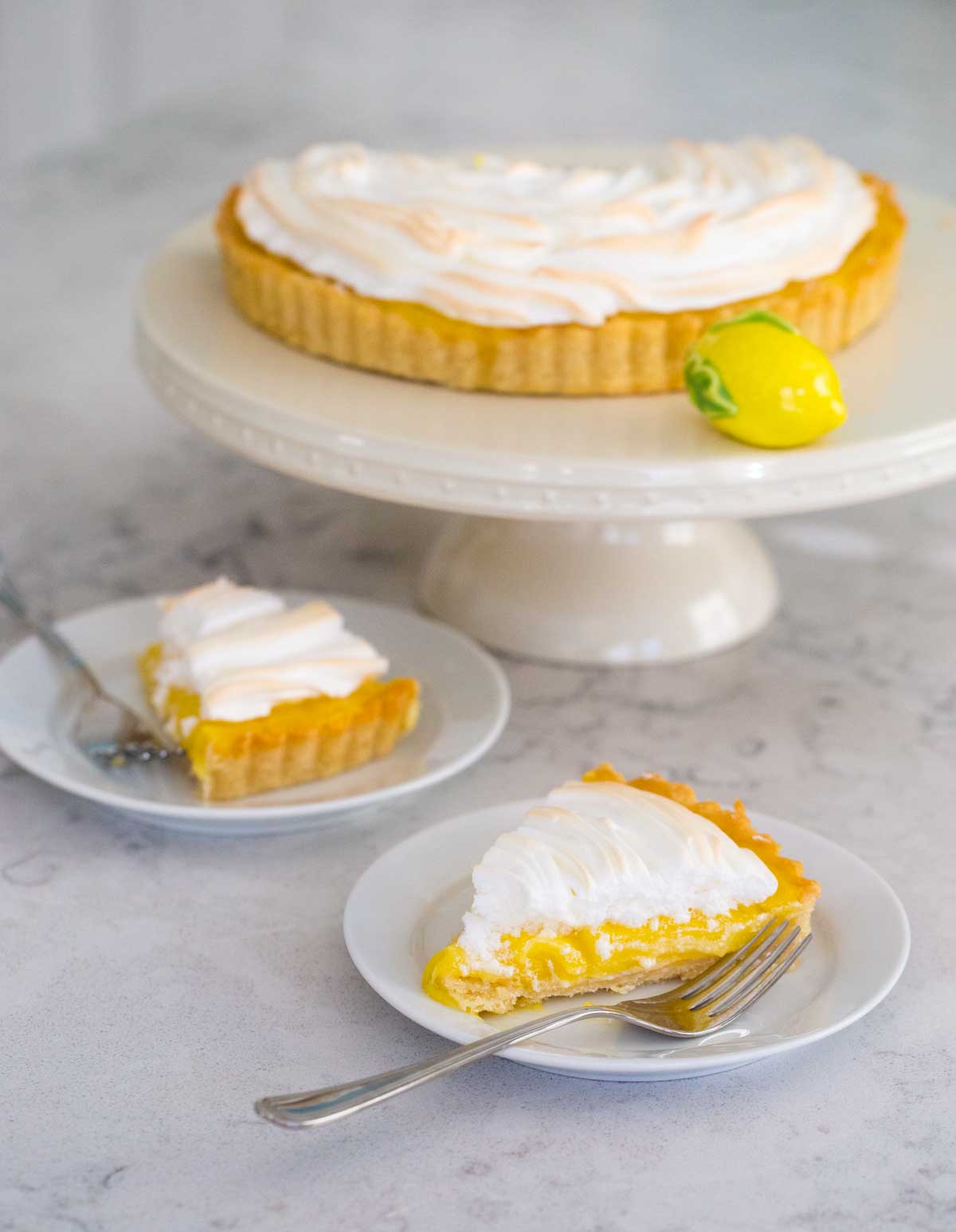 The finished lemon meringue tart is on a cake plate with two slices on smaller plates for serving.