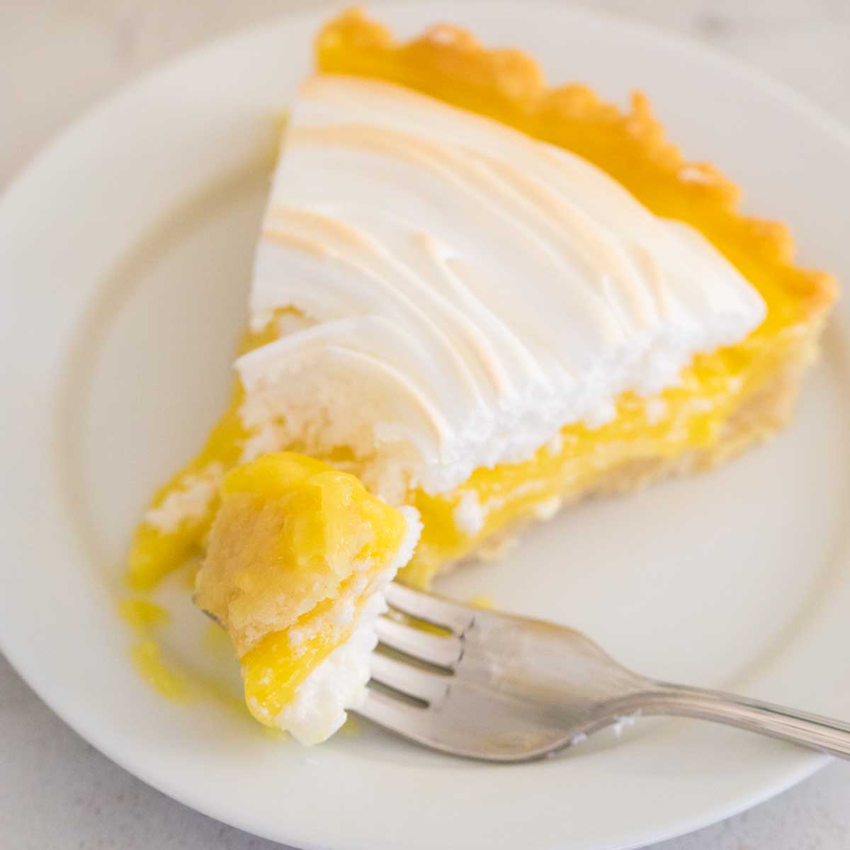 A slice of lemon meringue tart has a fork taking a bite.
