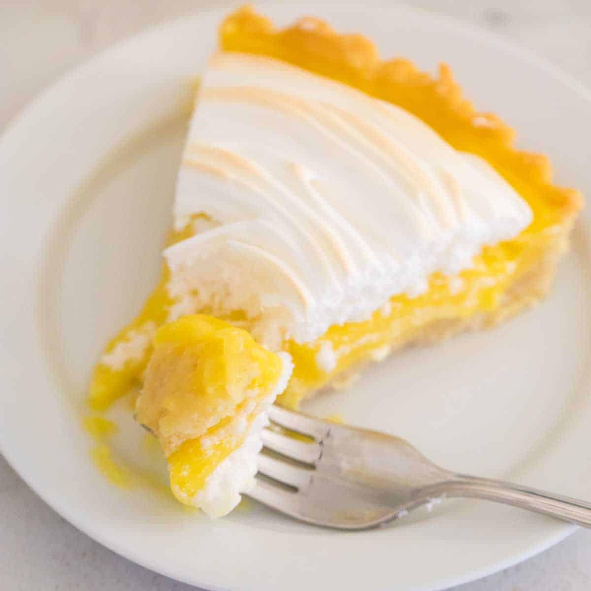 A slice of lemon meringue tart has a fork taking a bite.