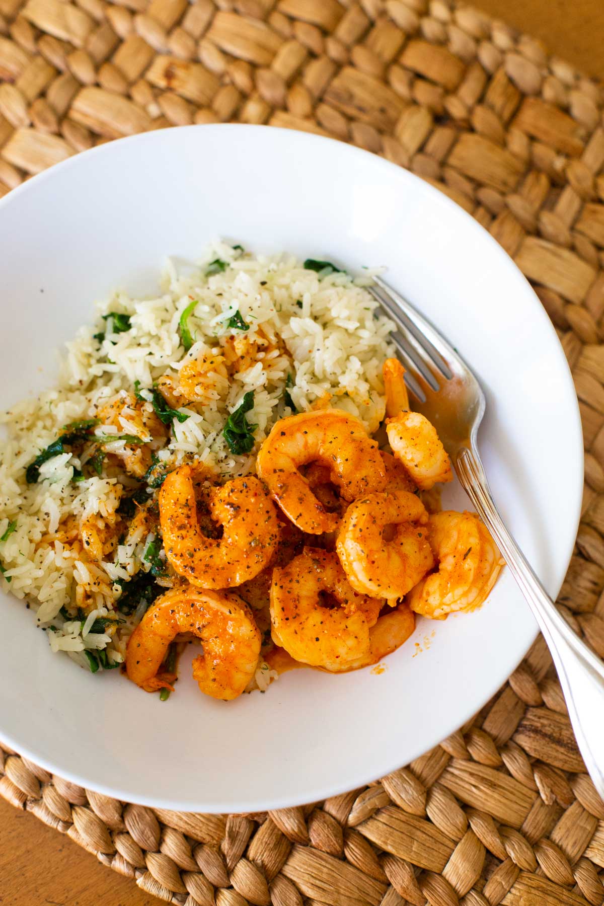 A serving bowl has a scoop of white rice with cooked spinach and seasoned shrimp on top.