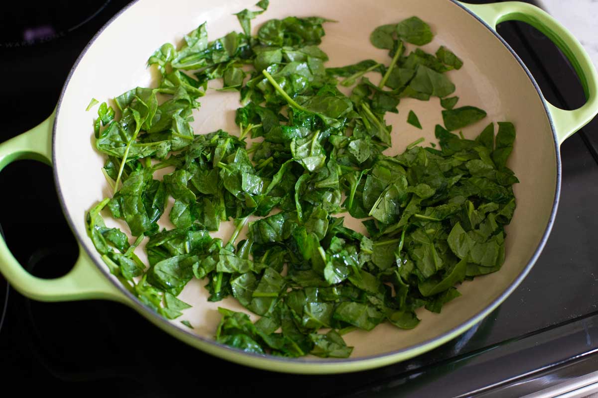 The fresh spinach is being cooked in a skillet.