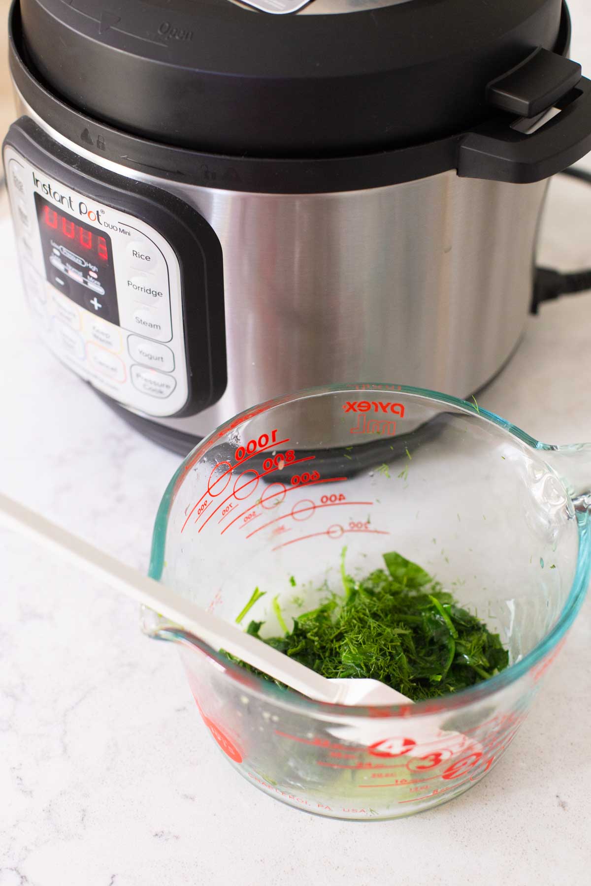 A measuring cup filled with cooked spinach and fresh dill waits by the Instant Pot.