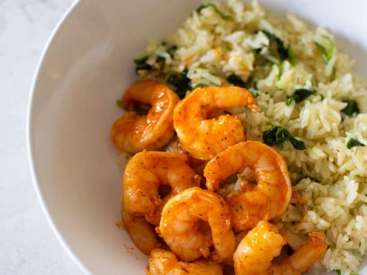 A bowl filled with white rice, spinach, and seasoned shrimp.