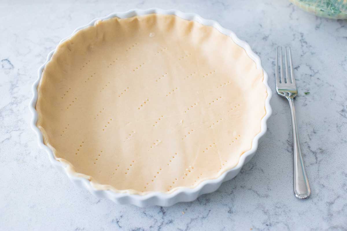 The quiche pan has been filled with a Pillsbury pie crust and pricked with a fork.