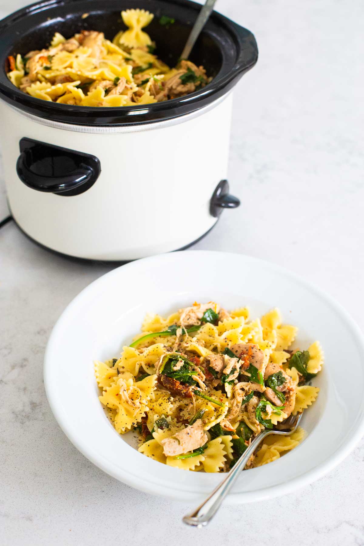 A serving of the Tuscan chicken pasta sits on the counter in front of the CrockPot that cooked it.
