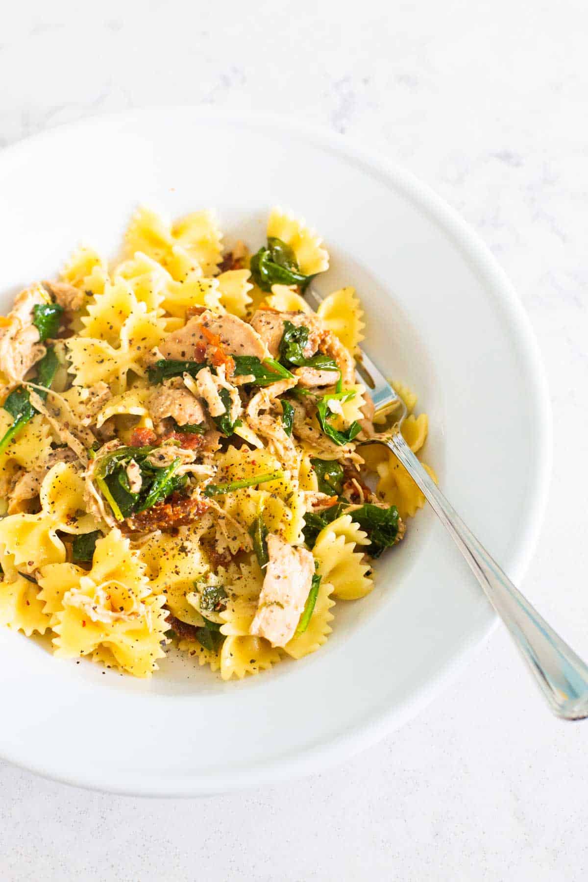 A white bowl filled with bowtie pasta and chicken.