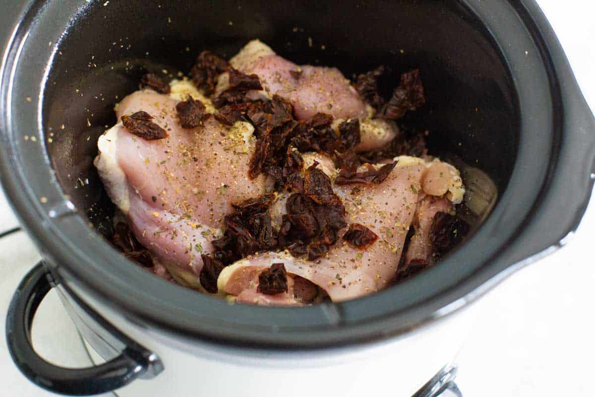 The chicken thighs and chopped sundried tomatoes have been seasoned inside the CrockPot.