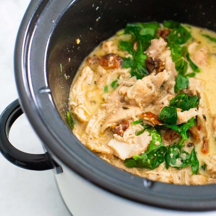 A CrockPot has a batch of Tuscan chicken with sundried tomatoes and spinach.