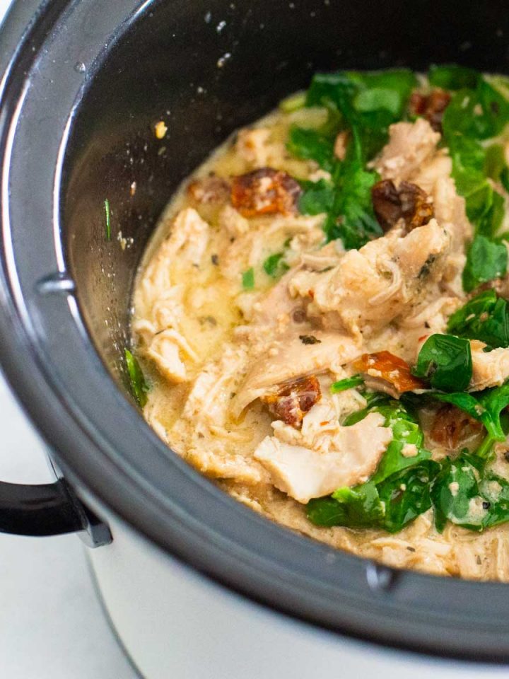 A CrockPot has a batch of Tuscan chicken with sundried tomatoes and spinach.