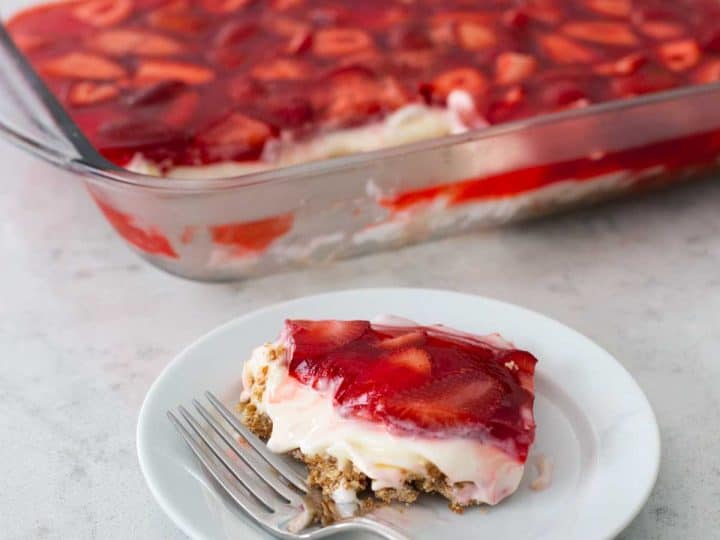 A 9x13-inch pan has finished strawberry pretzel salad for serving, a plate with a single slice and a fork is in front.