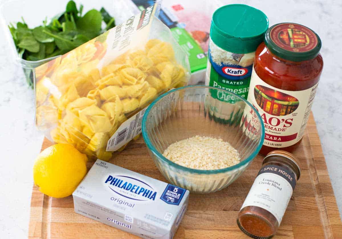 The ingredients to make baked tortellini are on a cutting board.