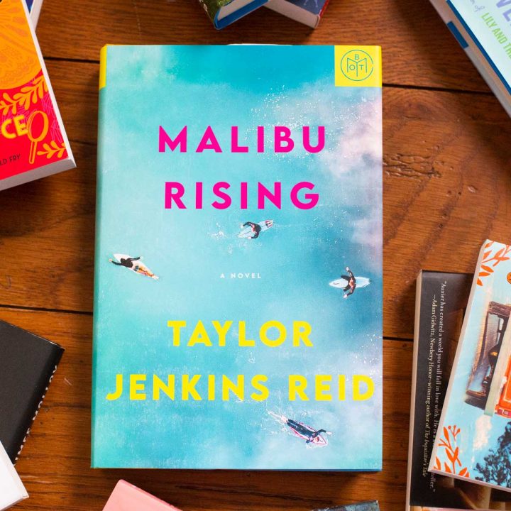 A copy of Malibu Rising sits on a table surrounded by books.