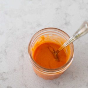 A super easy homemade buffalo sauce sits in a mason jar with a spoon.