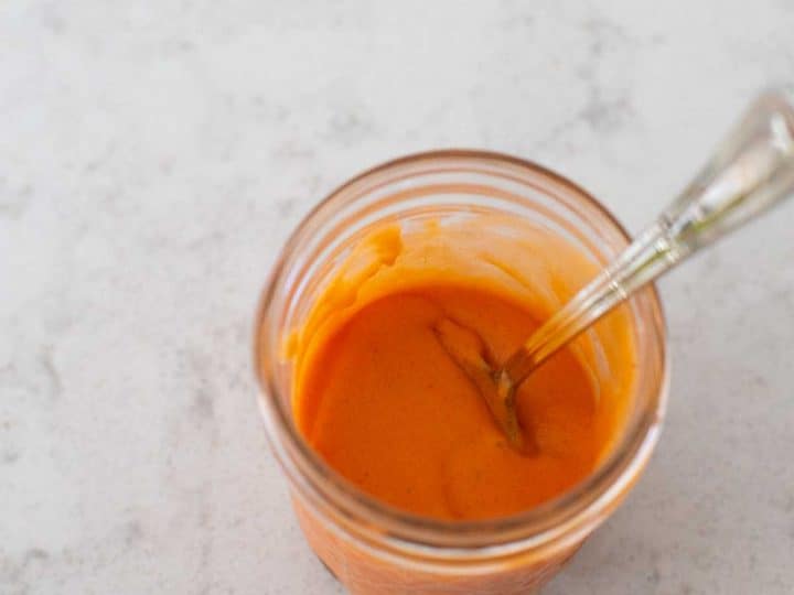 A super easy homemade buffalo sauce sits in a mason jar with a spoon.