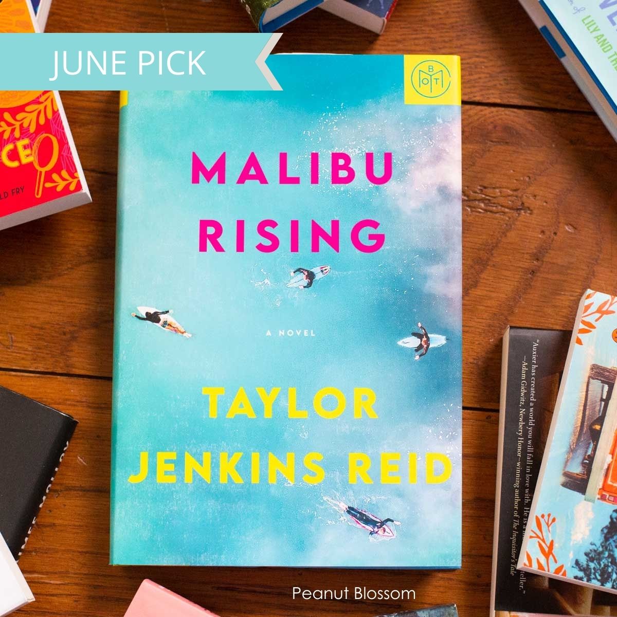 A copy of Malibu Rising sits on a table surrounded by books.