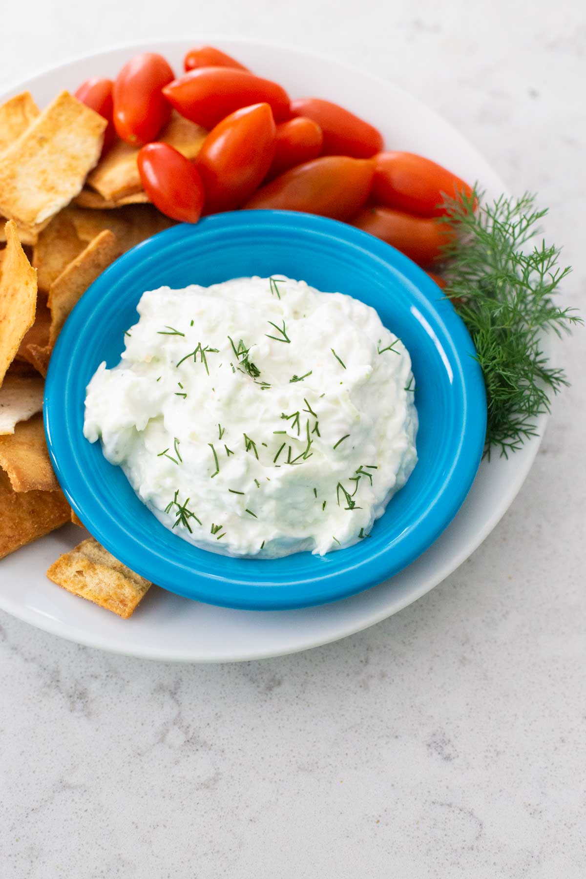 A bowl of tzatziki sauce is served with fresh tomatoes and pita chips.