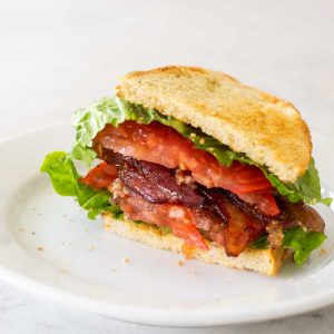 A perfect BLT sandwich sits on a white plate.