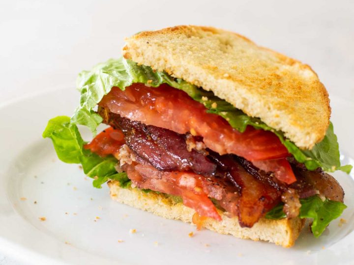 A perfect BLT sandwich sits on a white plate.