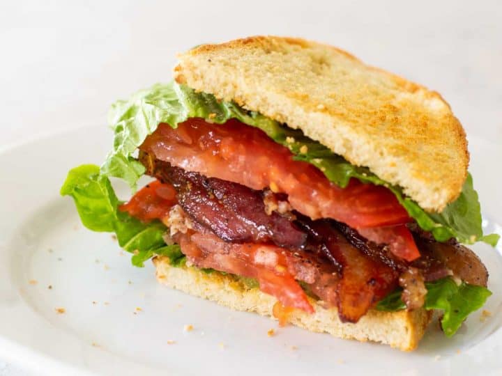 A perfect BLT sandwich sits on a white plate.