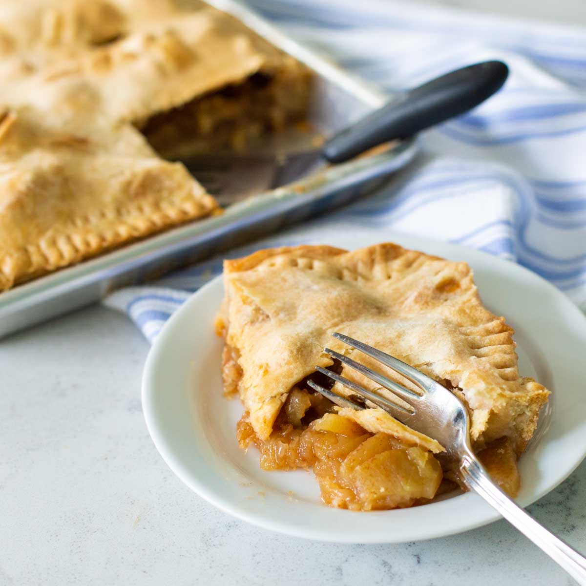 A square piece of apple pie has a fork taking a bite.