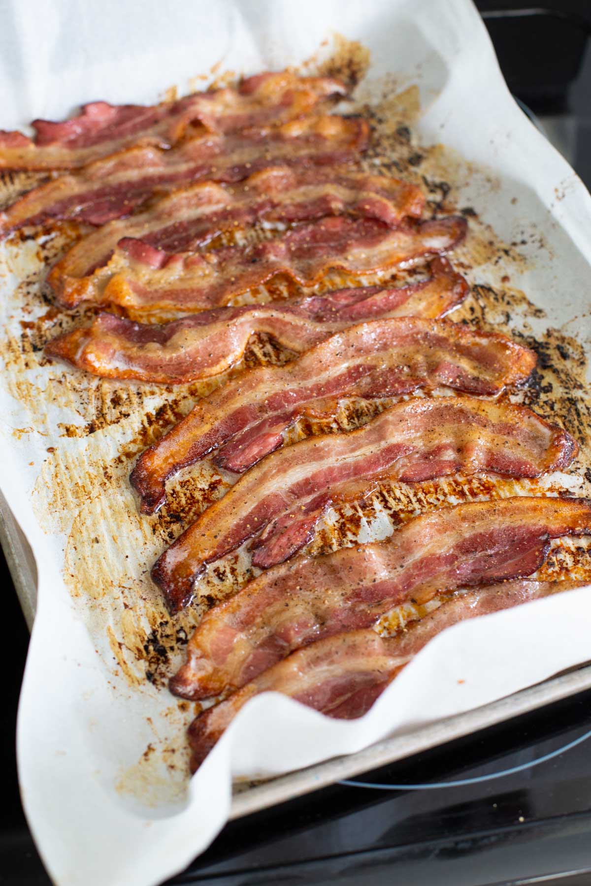 The bacon has been flipped, peppered, and is now crispy brown.