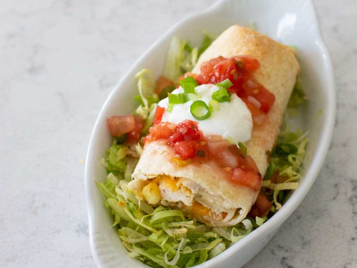 A crispy chimichanga has been sliced open to show the melted cheese inside. Sour cream and salsa are on top.