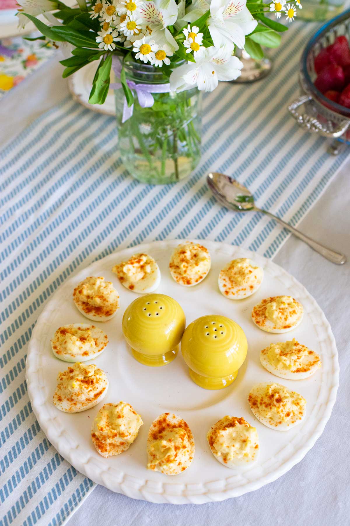 A platter of deviled eggs have a yellow salt and pepper shaker in the center.