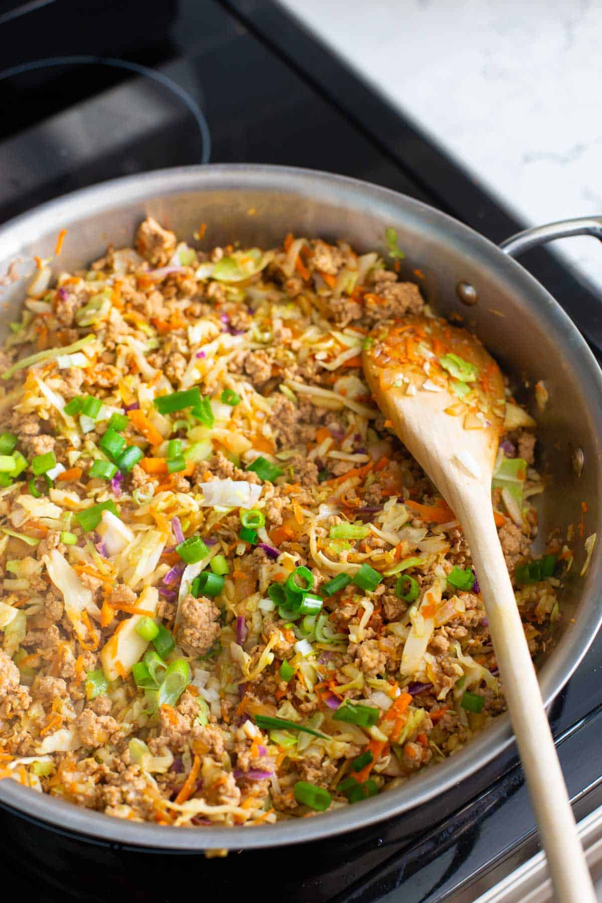 The finished egg roll recipe is in a large metal skillet with a wooden spoon.