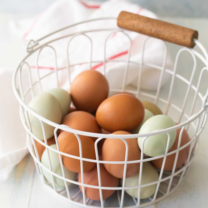 A basket of brown and blue eggs sit nexts to a towel.