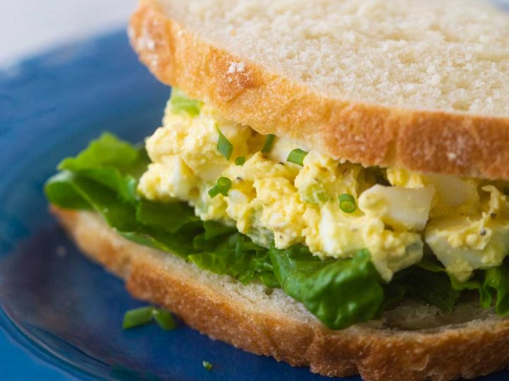 An egg salad sandwich sits on a blue plate.