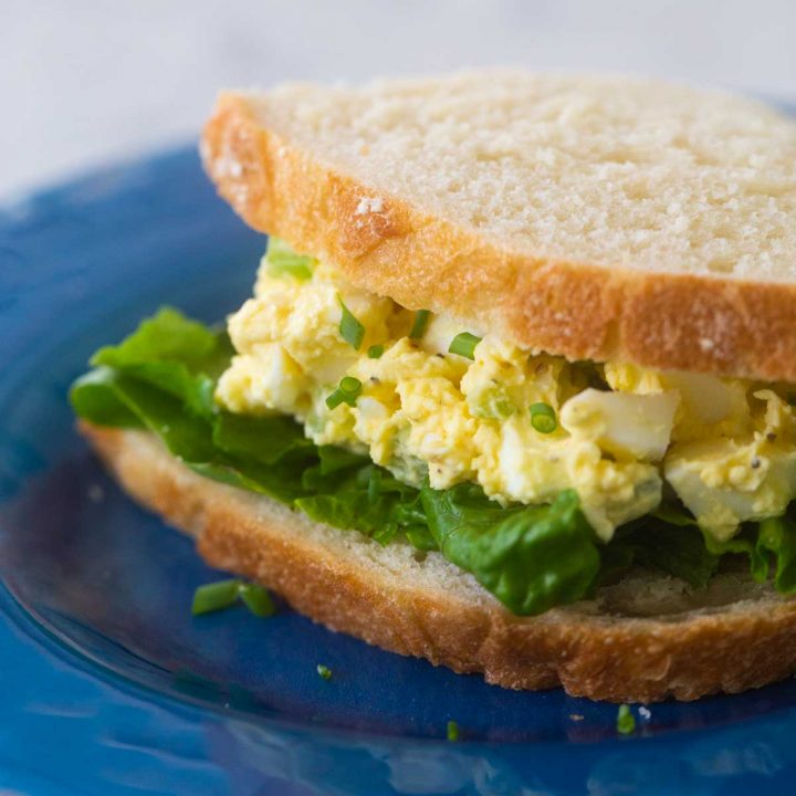 An egg salad sandwich sits on a blue plate.