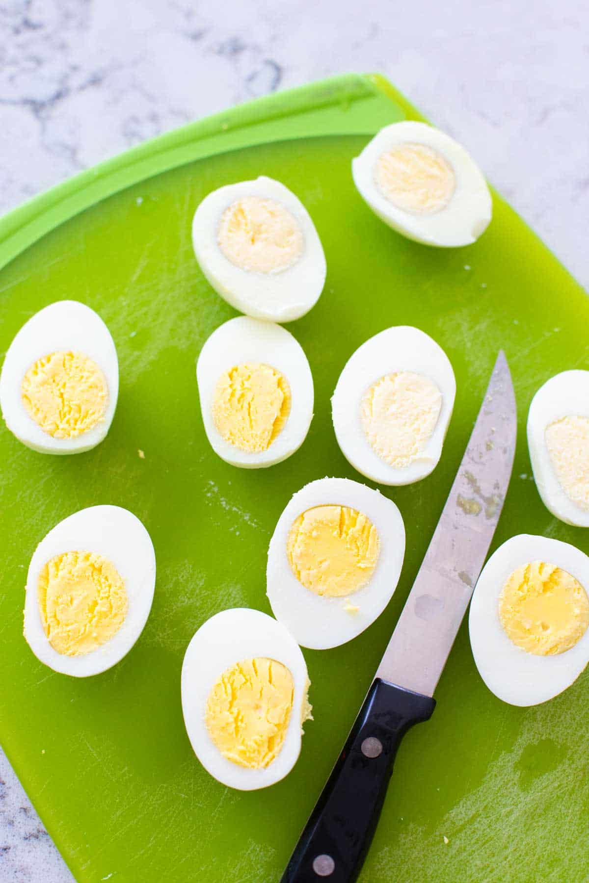 A cutting board has several hard boiled eggs that have been sliced in half so you can see the perfectly cooked egg yolks.