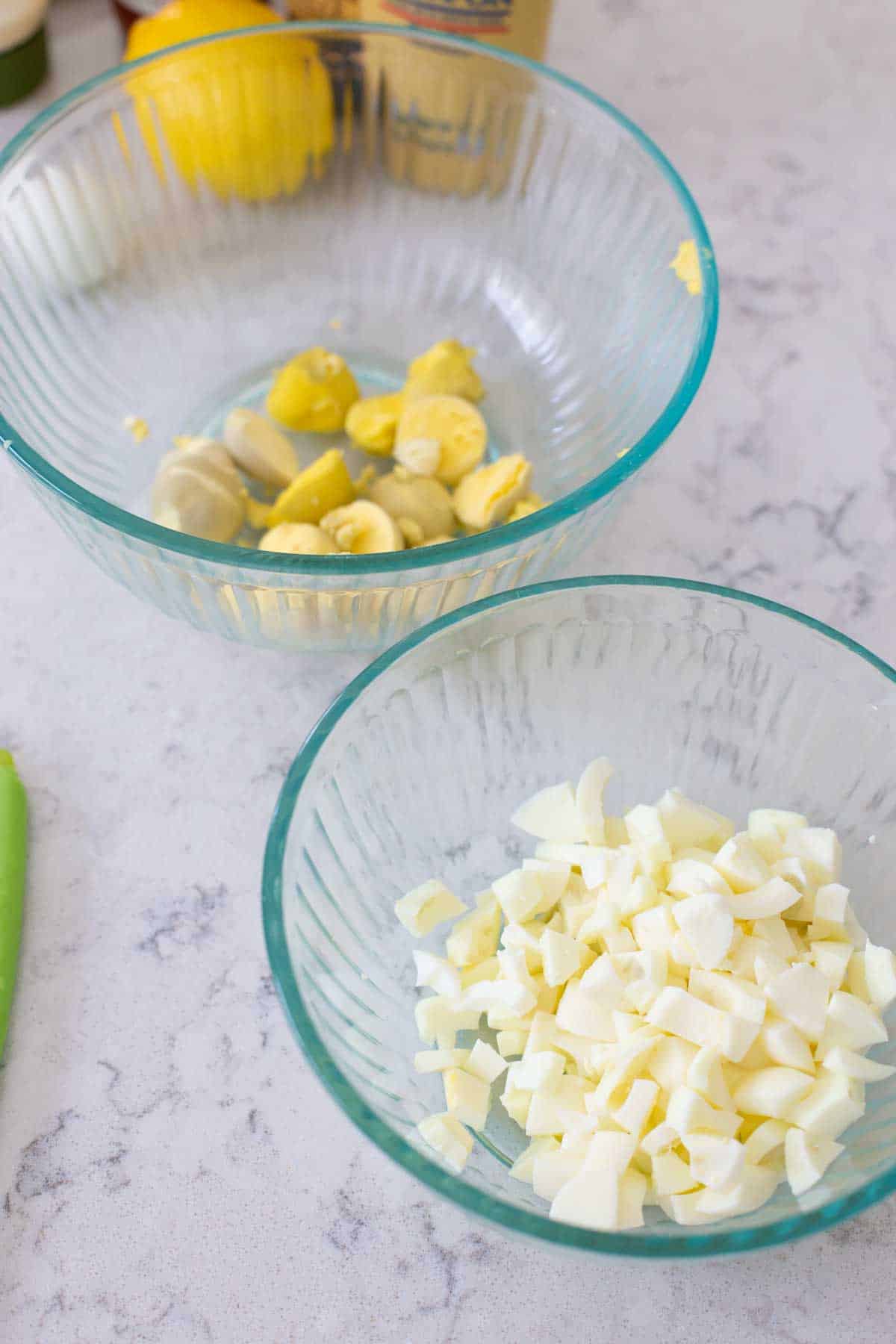 Two mixing bowls are side by side. One has the chopped egg whites, the other has the egg yolks.