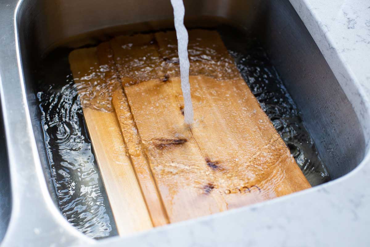 Cedar planks are soaking in water in a kitchen sink.