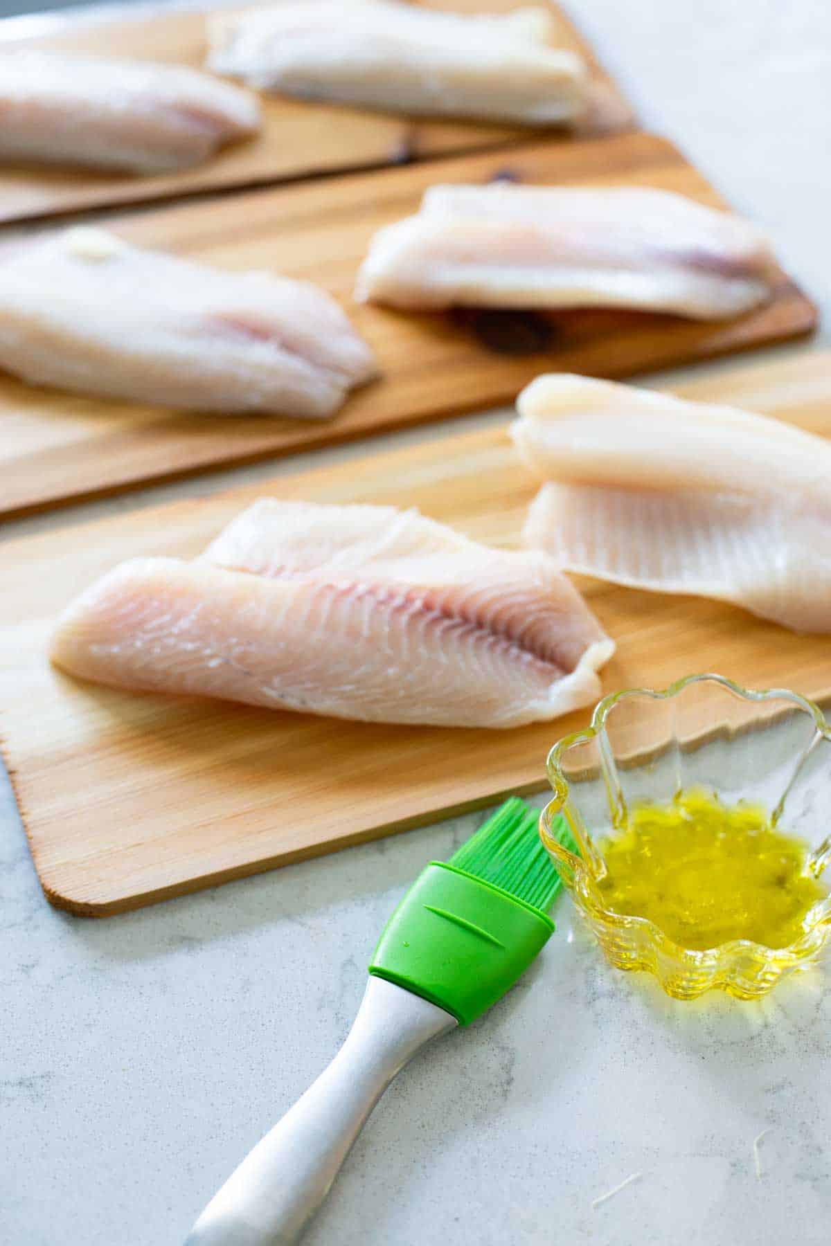 The tilapia are in a single layer on the cedar planks and a pastry brush is ready to brush them with olive oil.