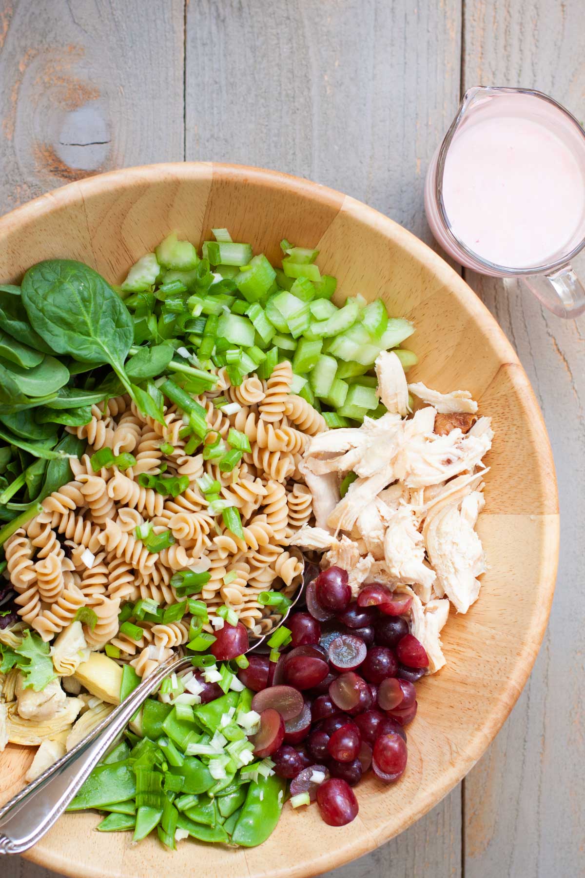 The ingredients for the pasta salad are in a mixing bowl with a pitcher of dressing on the side.