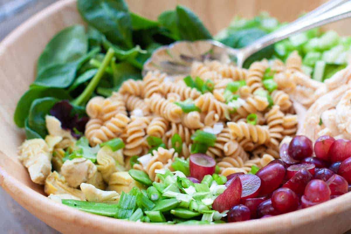 Baby spinach, rotini noodles, red grapes, and chopped veggies are ready to be mixed.