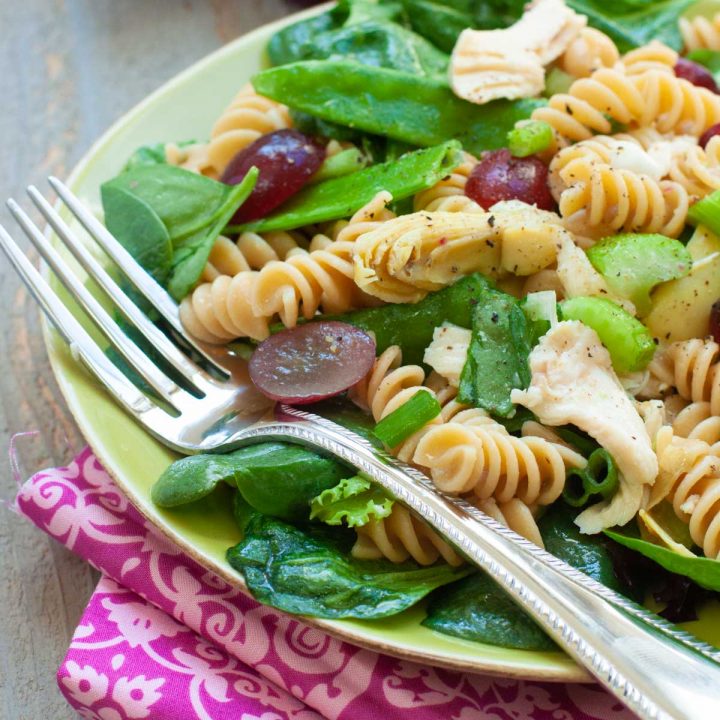 A serving of grape and chicken pasta salad is on a plate with a fork.