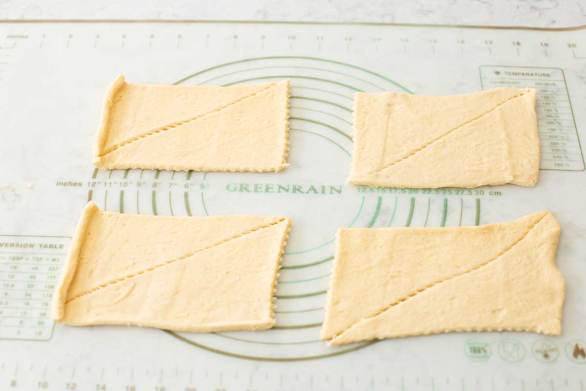 4 unrolled portions of crescent dough are laid on a baking mat.