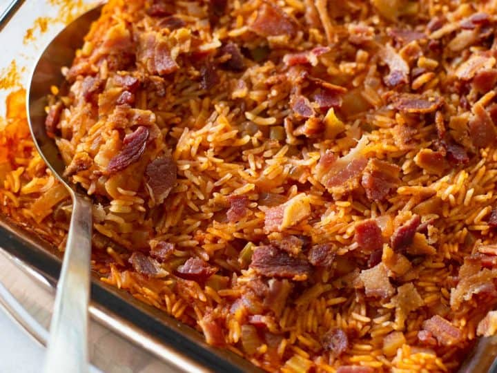 The finished baked rice dish with tomato and bacon has a spoon ready to serve.