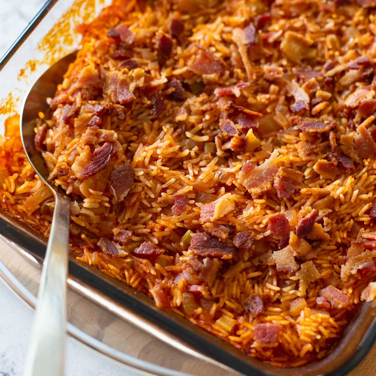 The finished baked rice dish with tomato and bacon has a spoon ready to serve.