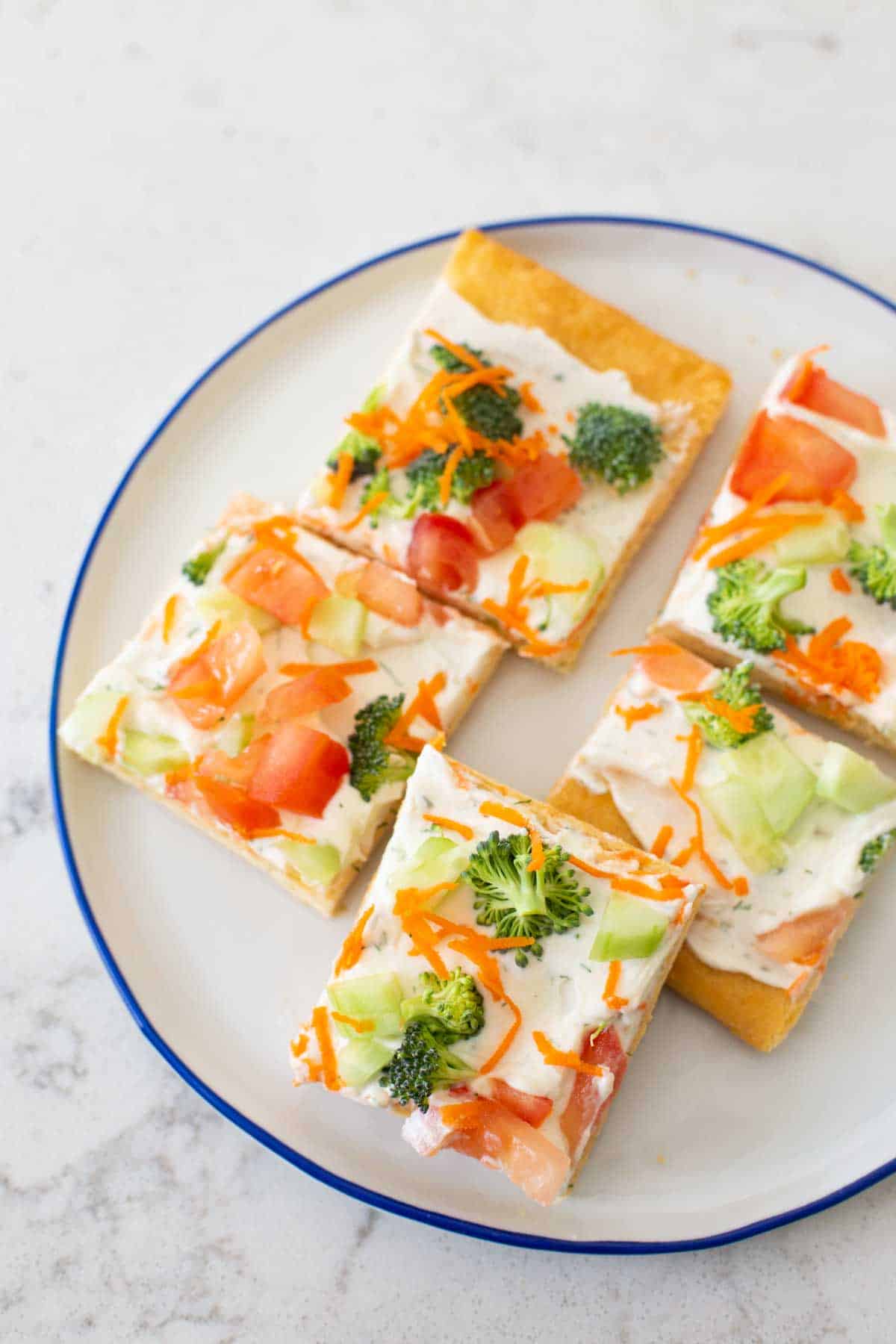 A white plate with a blue rim has several portions of veggie pizza ready to serve.