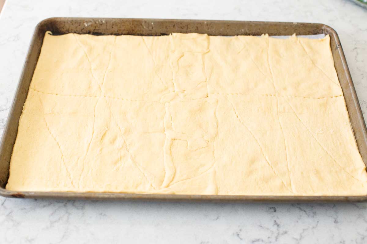 An even layer of crescent roll dough has been spread in a baking pan.