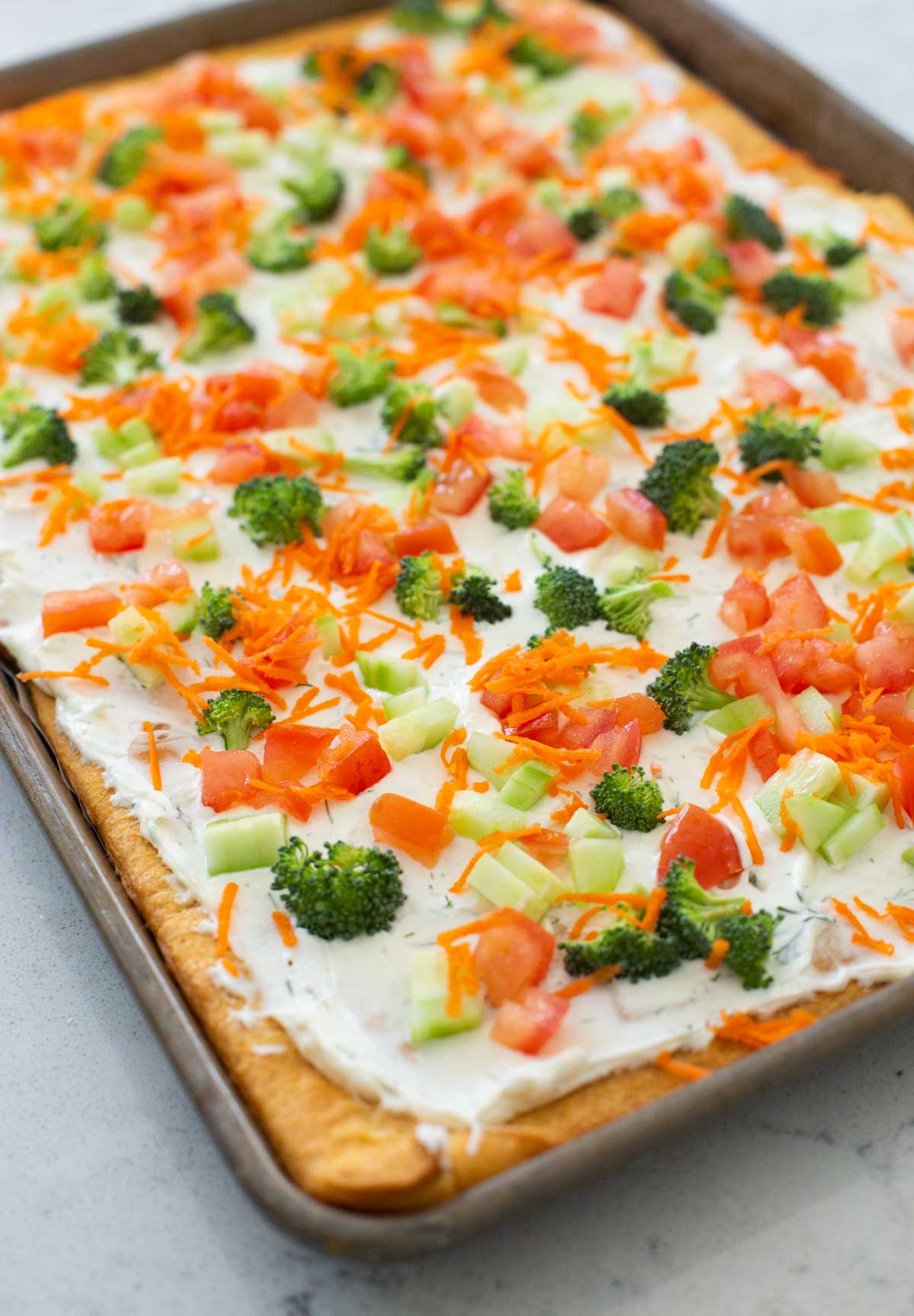 The raw veggie pizza is fully assembled and the vegetables have been gently patted into the cream cheese.