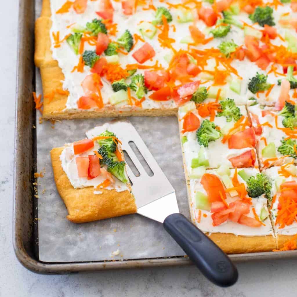 A veggie pizza has been sliced and served with a small spatula.